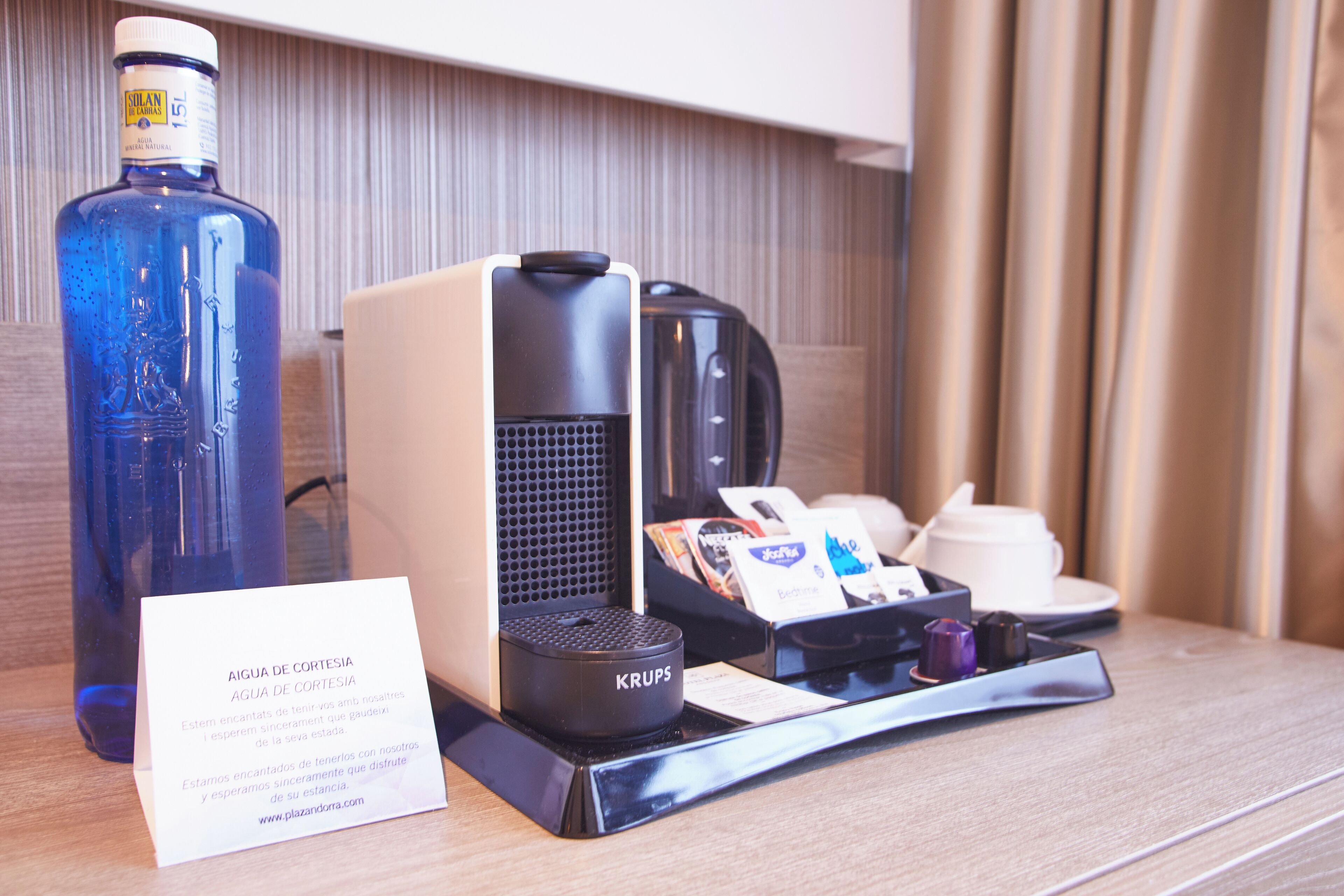 A hotel room with a coffee maker, a bottle of water, and a menu card on the table.