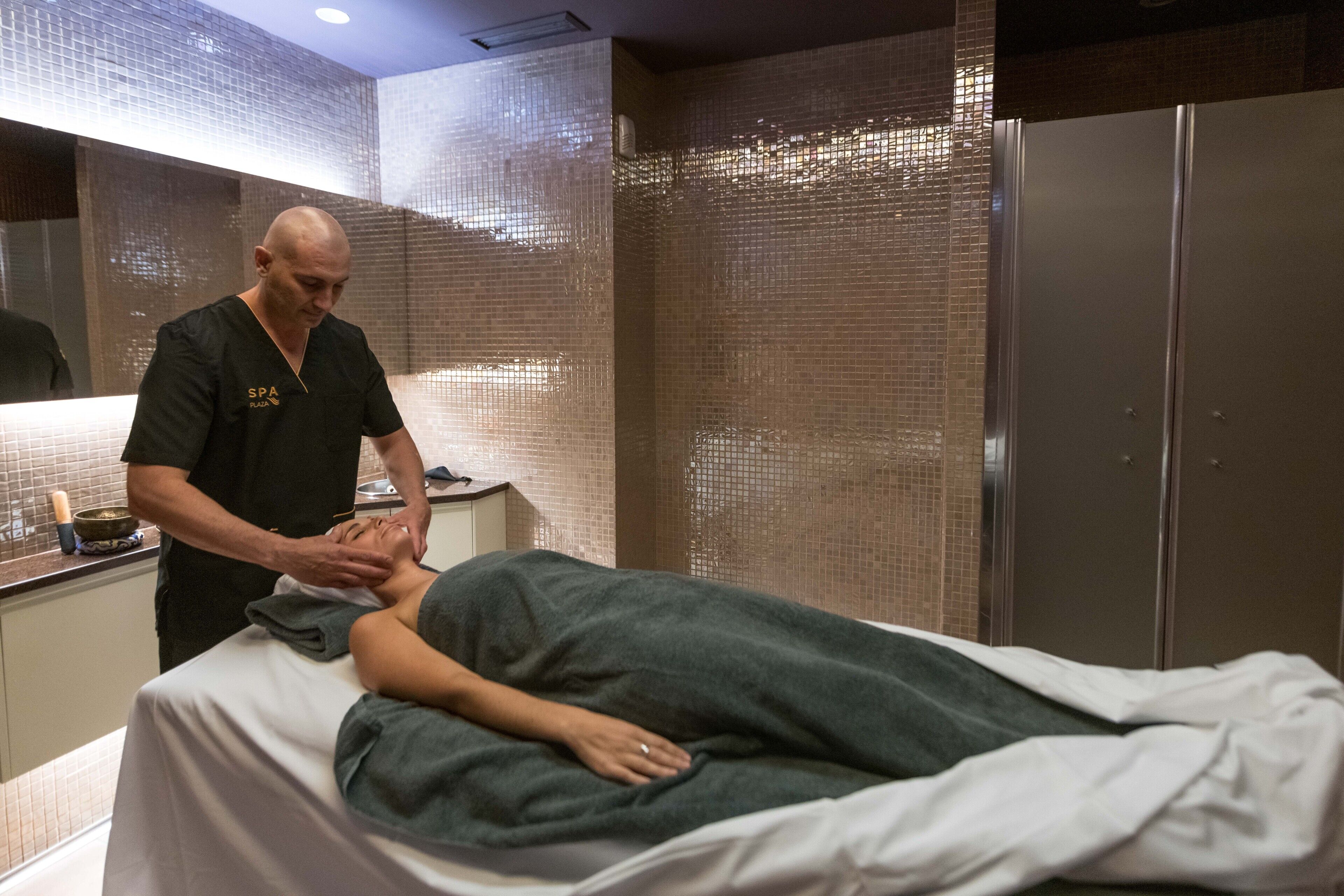 Un cuarto de tratamientos de spa con una camilla de masaje, un cliente recibiendo un masaje y un terapeuta.