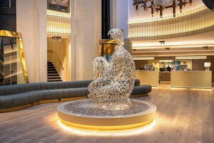 Un vestíbulo moderno con una escultura central, una escalera y un mostrador de recepción.