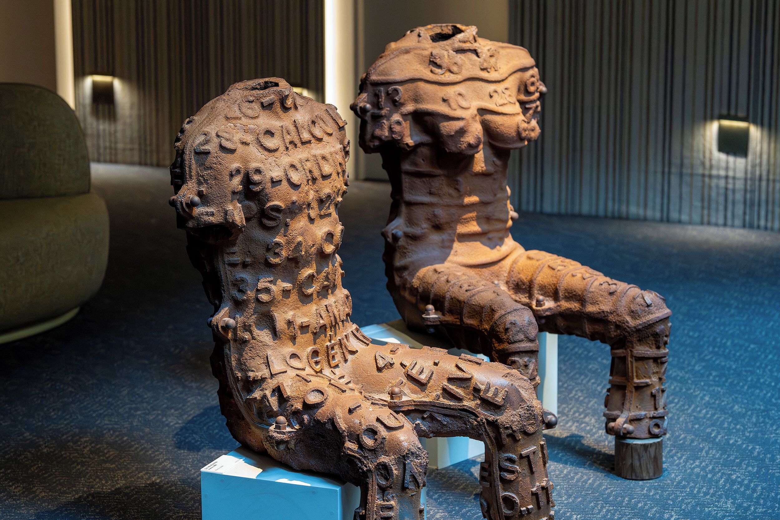 A sculpture of a seated figure with inscriptions, displayed on a pedestal.