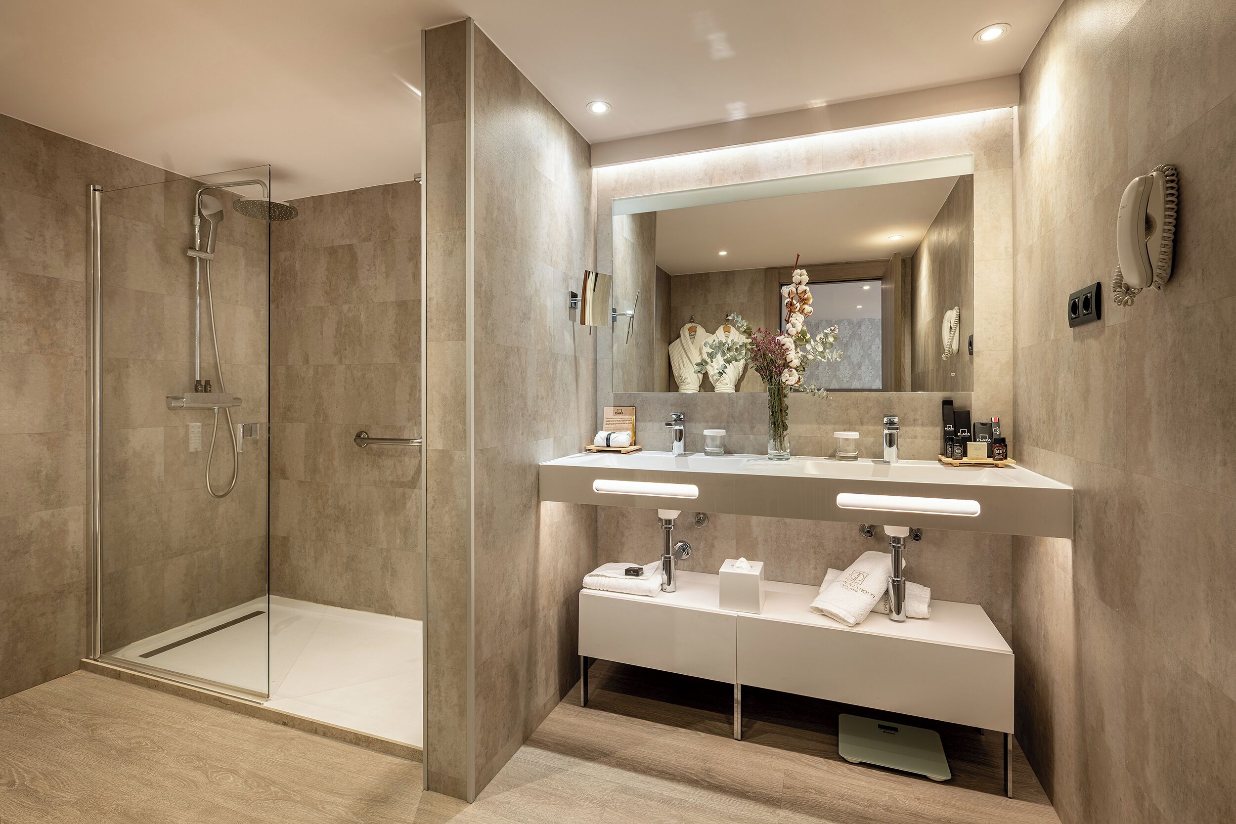 Un baño moderno con ducha envuelta en vidrio, tocador con dos lavamanos y un espejo grande.