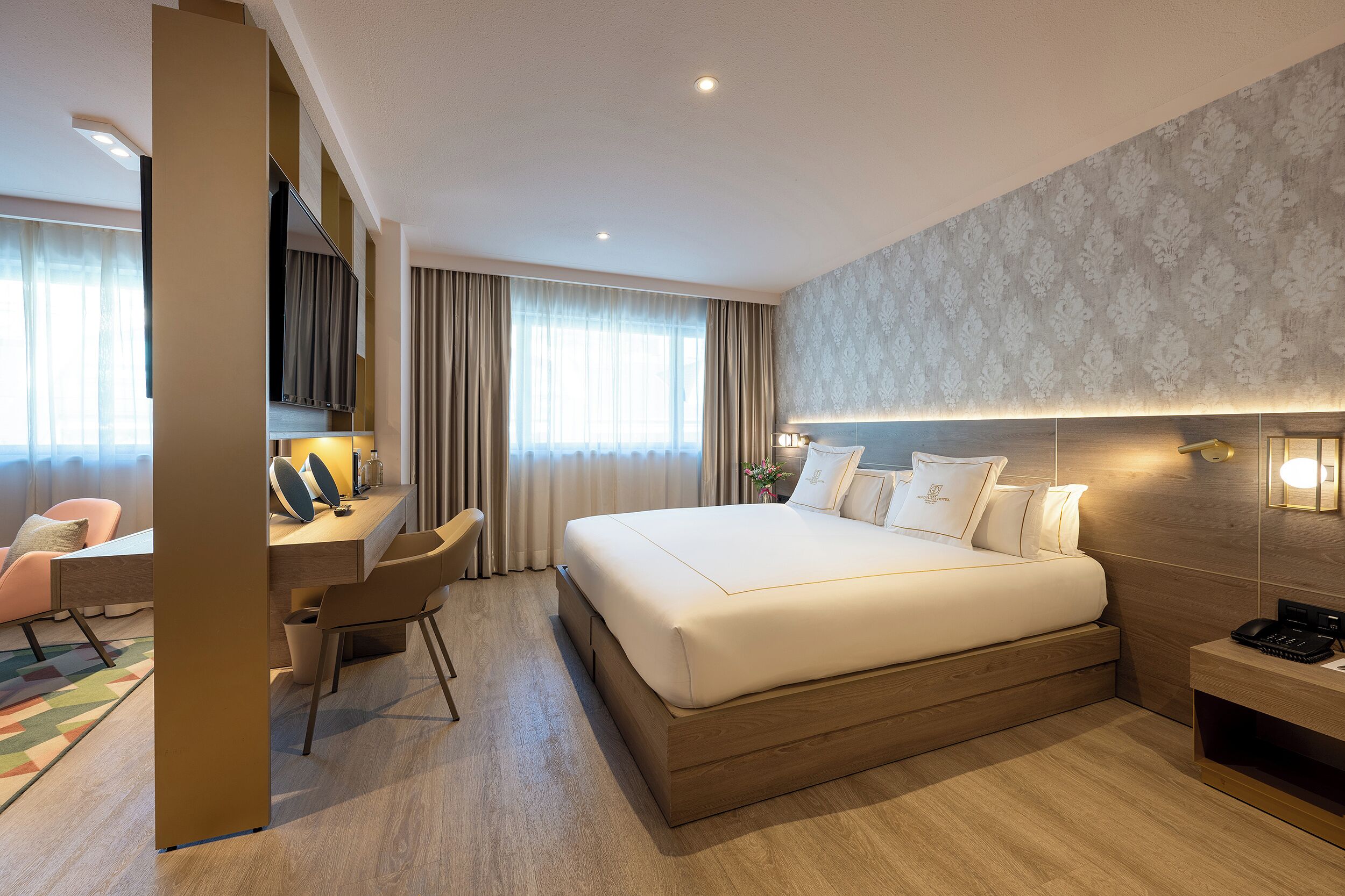 Ein Hotelzimmer mit einem großen Bett, einem Schreibtisch, einem Sessel, einem Nachttisch und einem an der Wand befestigten Fernseher.