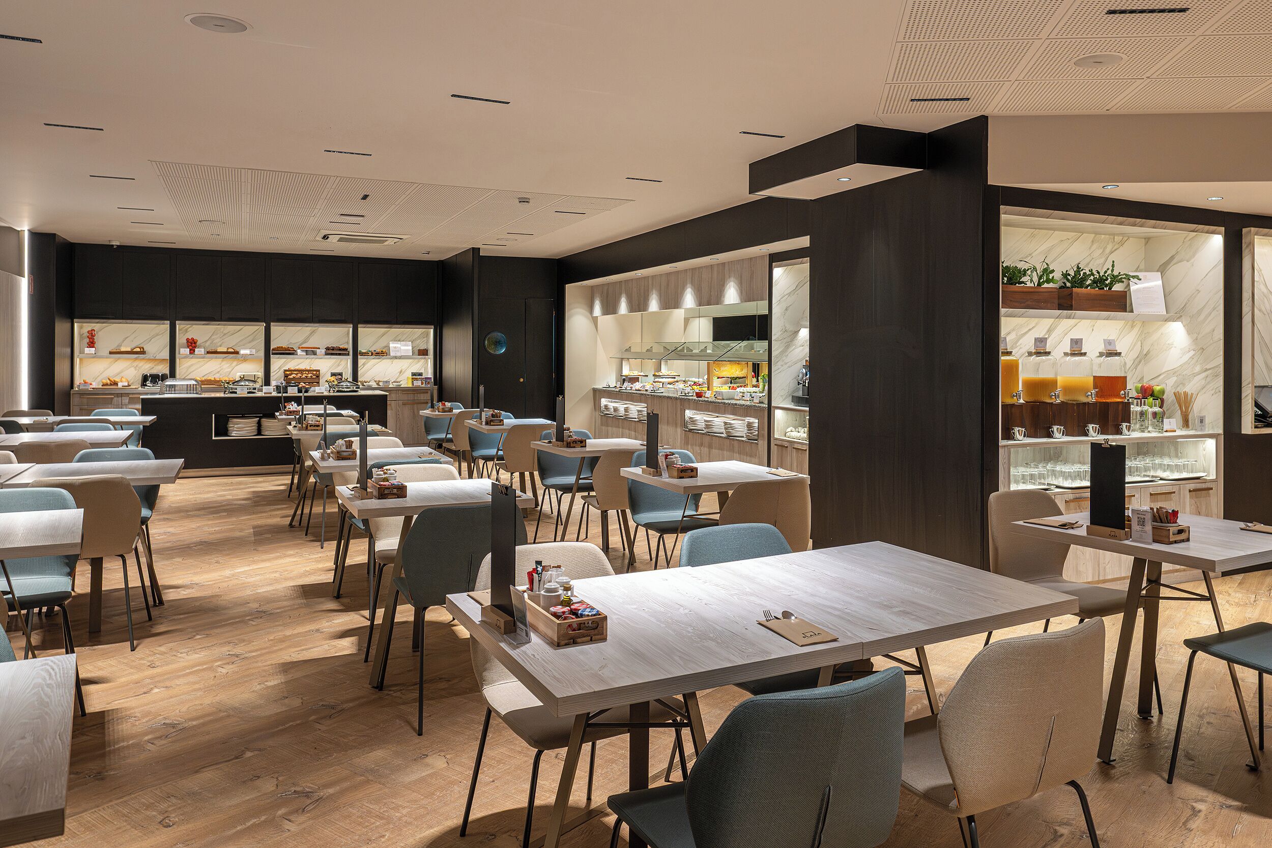 A modern restaurant with wooden tables and chairs, a bar area, and a display of food items.