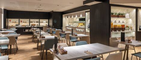 A modern restaurant with wooden tables and chairs, a bar area, and a display of food items.