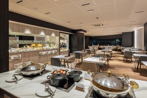 A modern dining area with multiple tables, a kitchen area with a buffet, and a large window providing natural light. -  Grand Plaza Hotel & Wellness (Andorra la Vella)