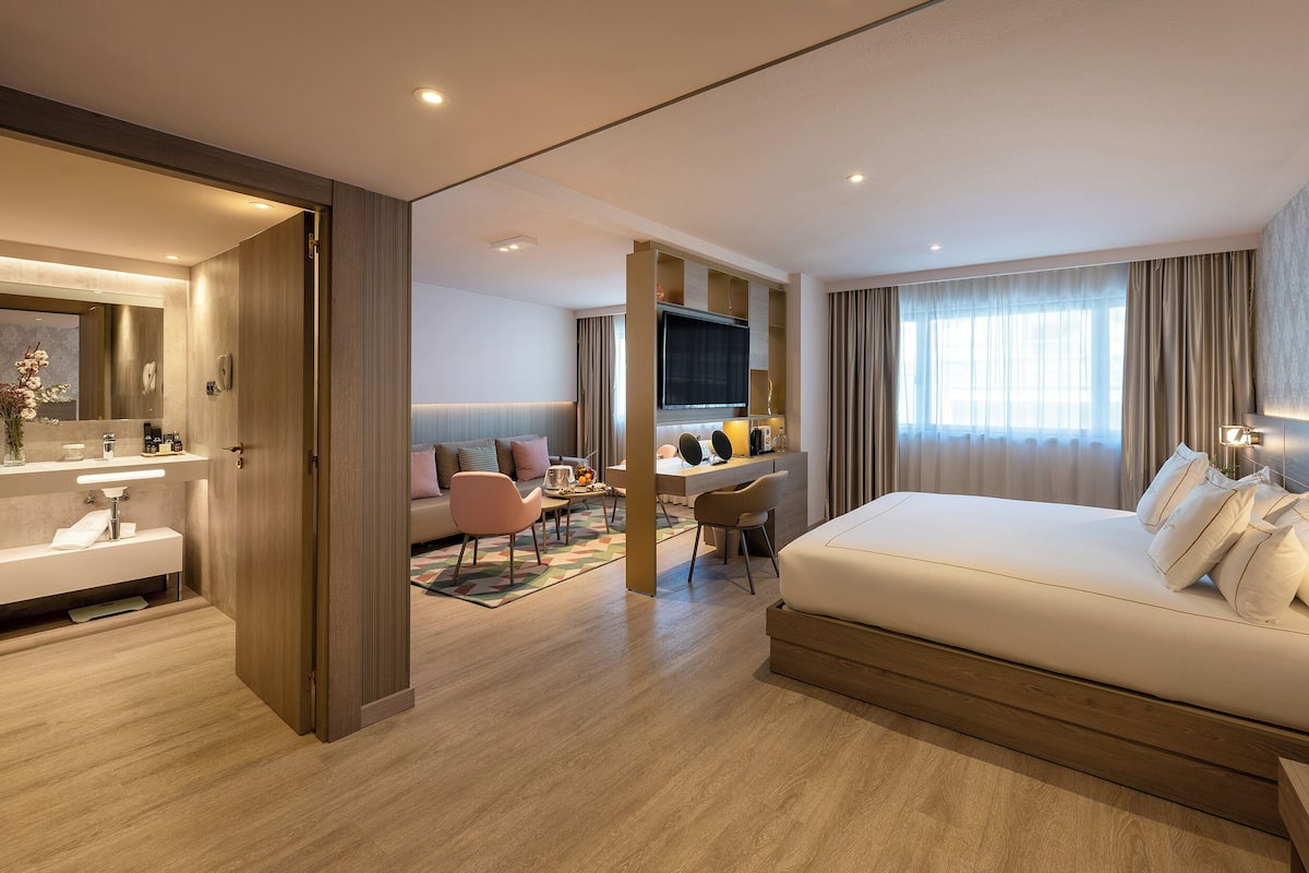 A modern hotel room with a large bed, a desk, a TV, and a bathroom.