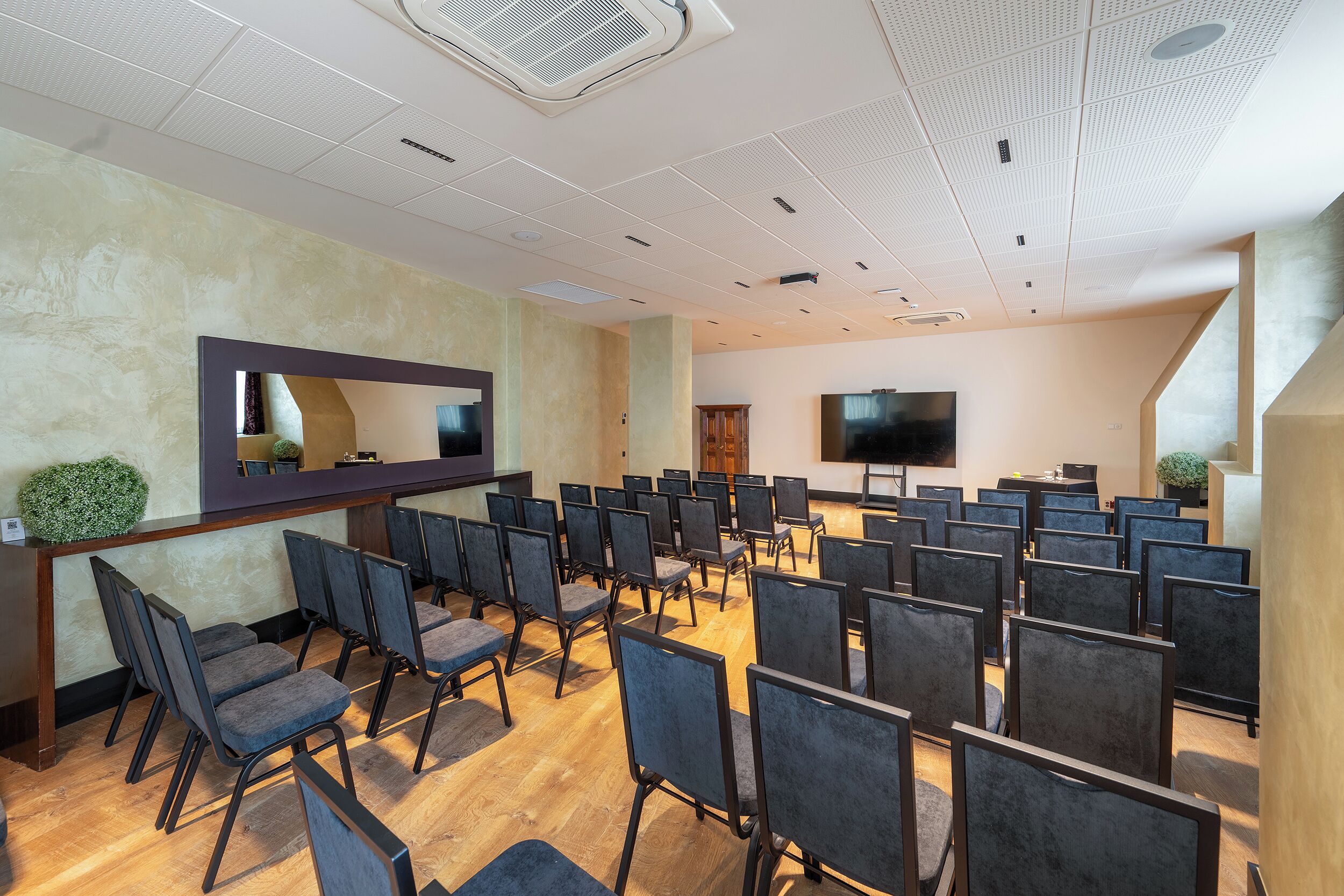 A conference room with rows of chairs, a large flat-screen TV, and a wooden reception desk.