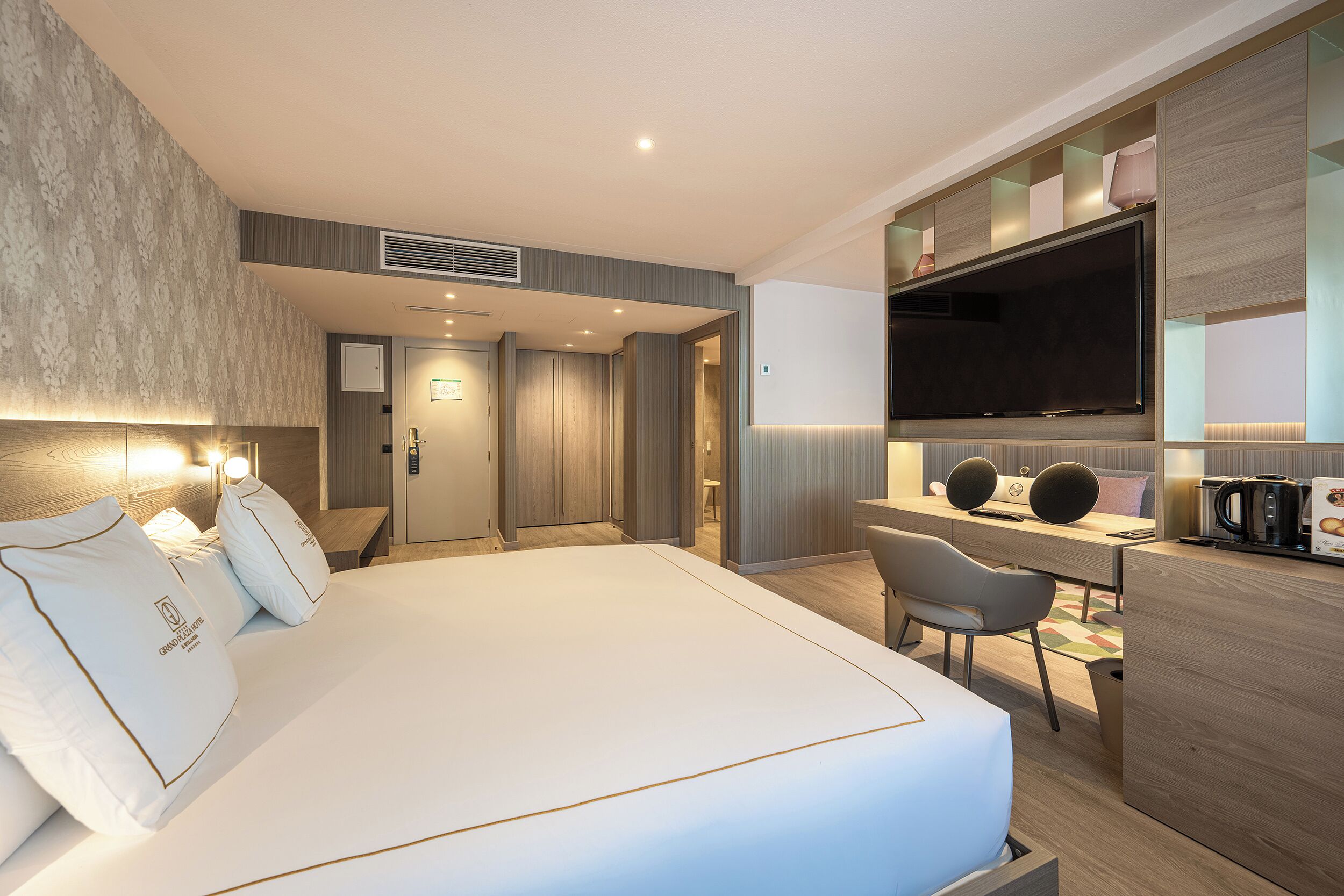 A modern hotel room with a large bed, a desk with a flat-screen TV, a coffee machine, and a seating area.