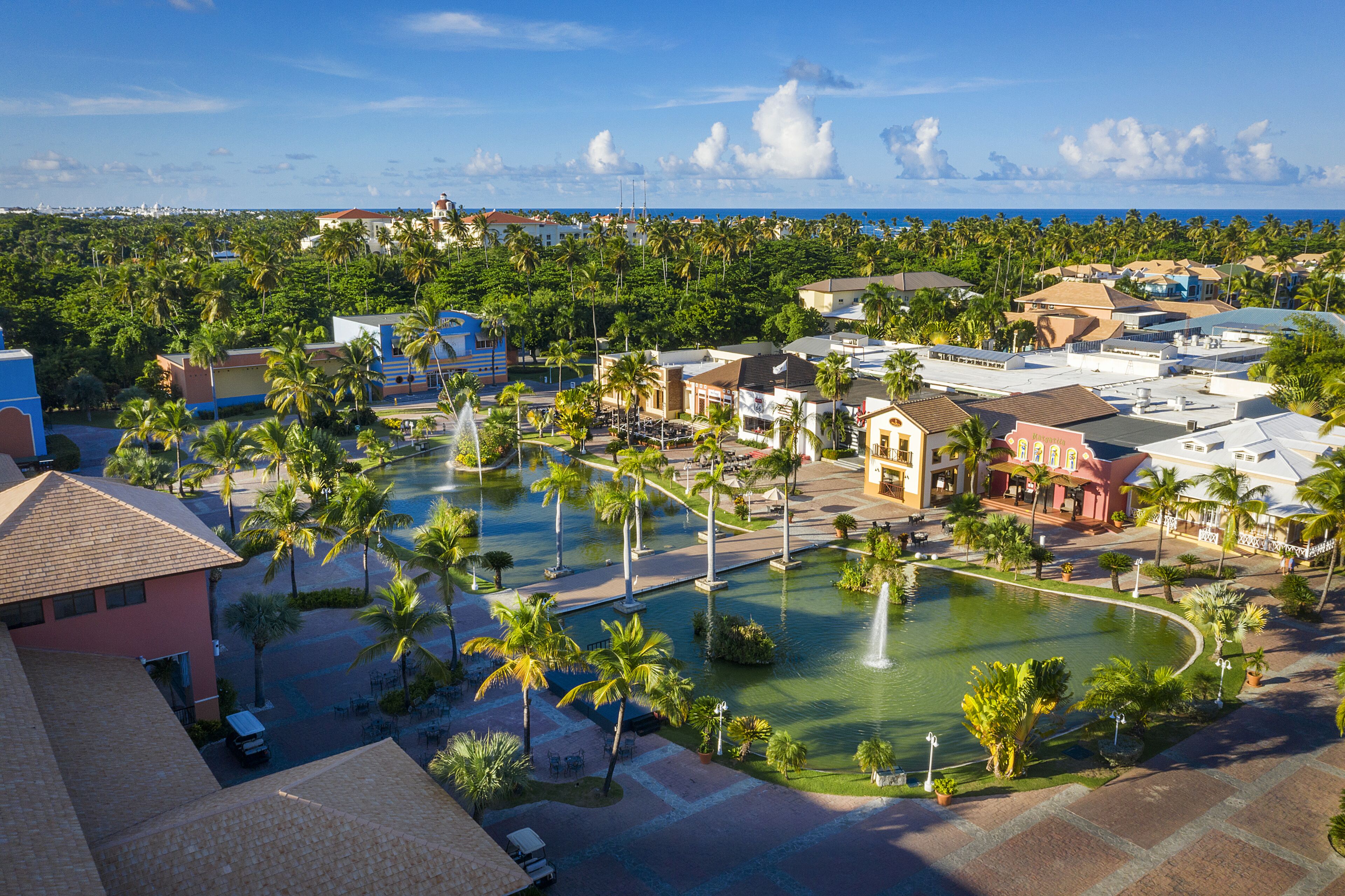 A resort with a central pool, palm trees, and a view of the ocean.