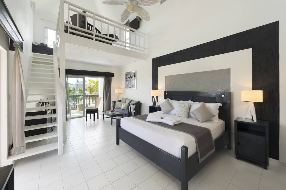 A bedroom with a large bed, a balcony, a desk, and a staircase.