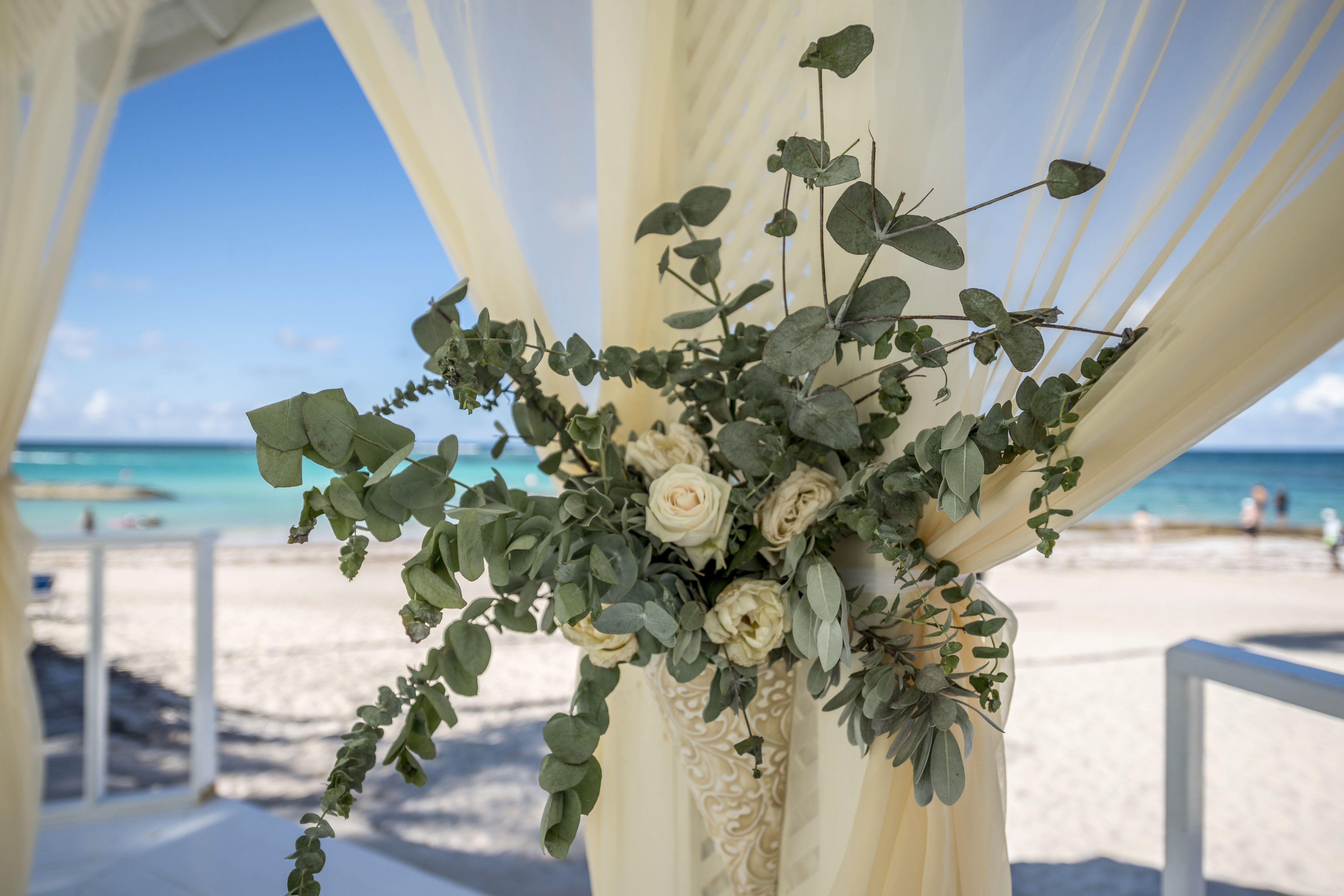 Une cérémonie de mariage organisée sur la plage, avec une composition florale placée sur une colonne blanche.