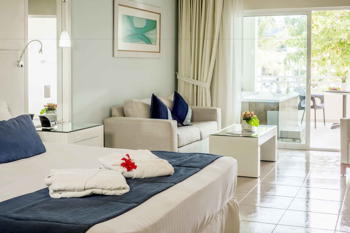 A hotel room with a bed, a sofa, a small table, and a view of the outdoors.
