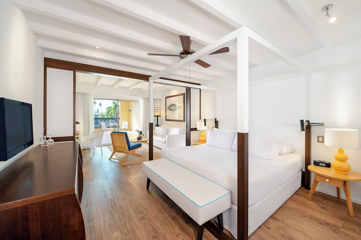 A hotel room with a large bed, a desk, a chair, a TV, and a ceiling fan.