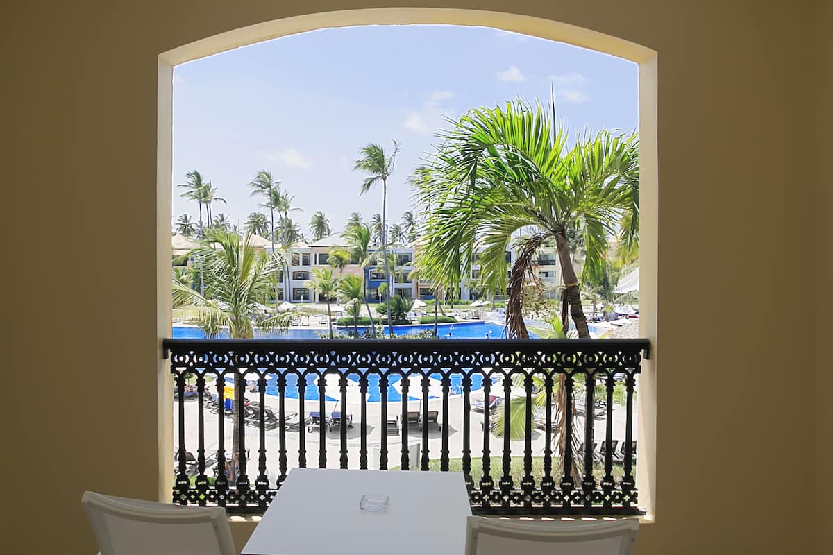 A balcony with a view of a pool area, palm trees, and a building with multiple balconies.