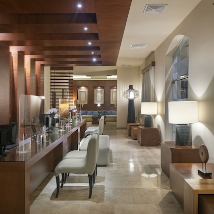 A modern hotel lobby with a reception desk, seating area, and large windows.