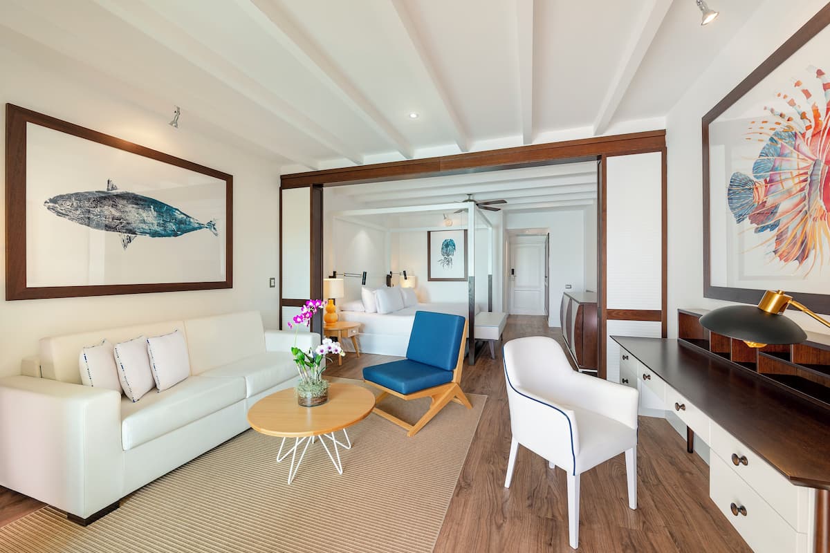 A modern living room with a white sofa, a blue armchair, a wooden coffee table, and a desk with a lamp.