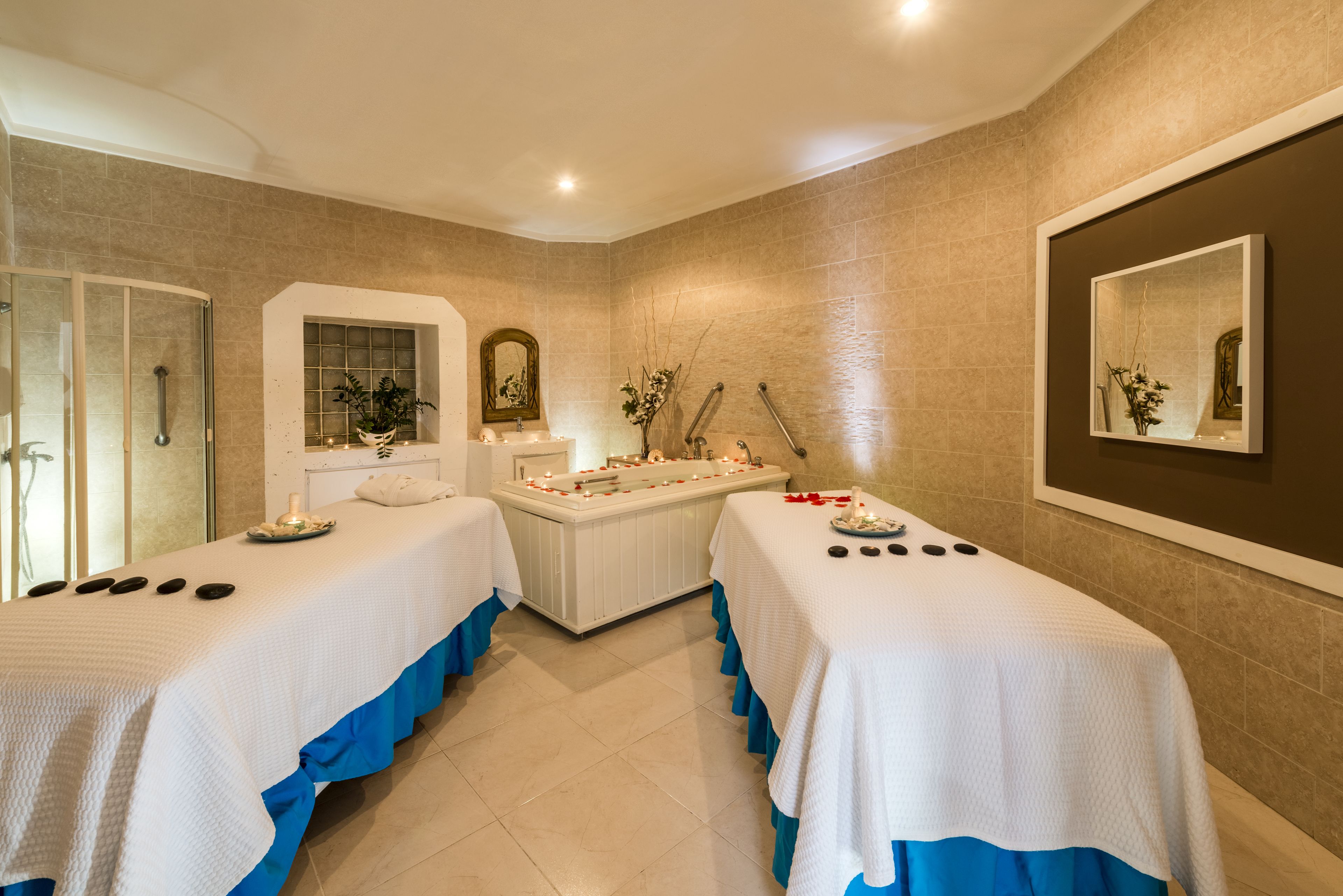 A spa room with two beds, a bathtub, and a mirror on the wall.