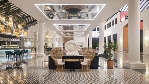 Un amplio vestíbulo con zona de bar, dos sillones de mimbre, una mesa redonda y una gran escultura decorativa.