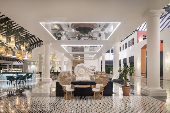 Un hall d’entrée spacieux avec un coin bar, deux fauteuils en osier, une table ronde et une grande sculpture décorative.