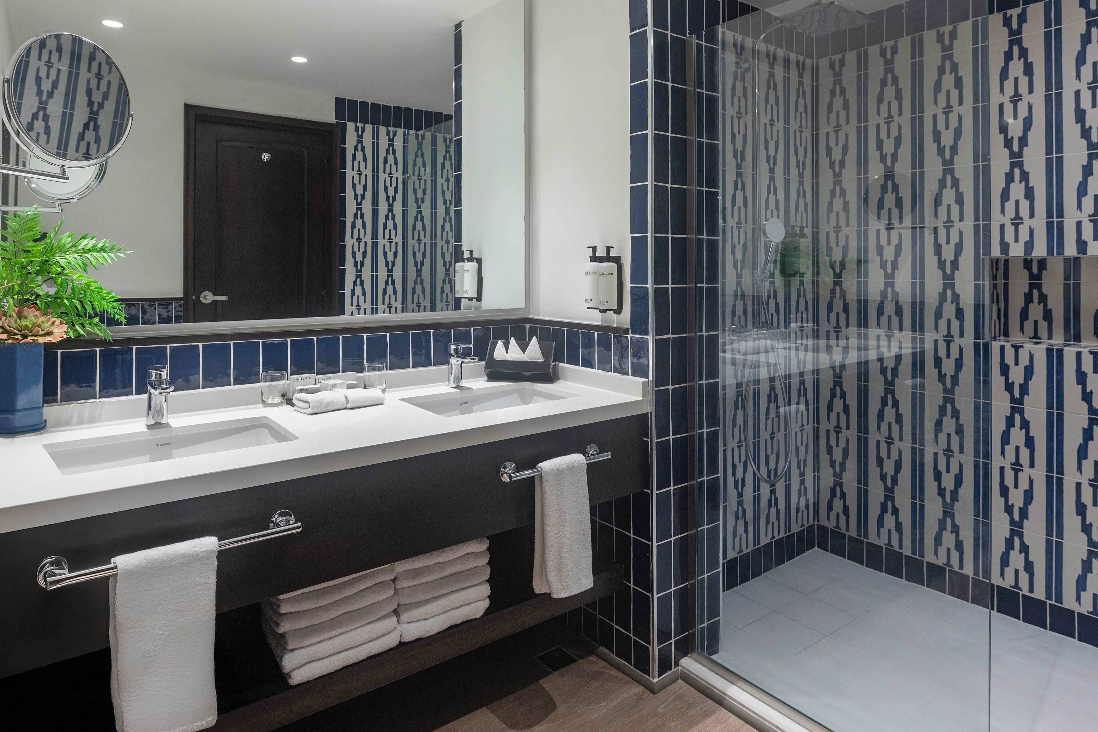 A modern bathroom with two sinks, a large mirror, and a shower area with patterned tiles.