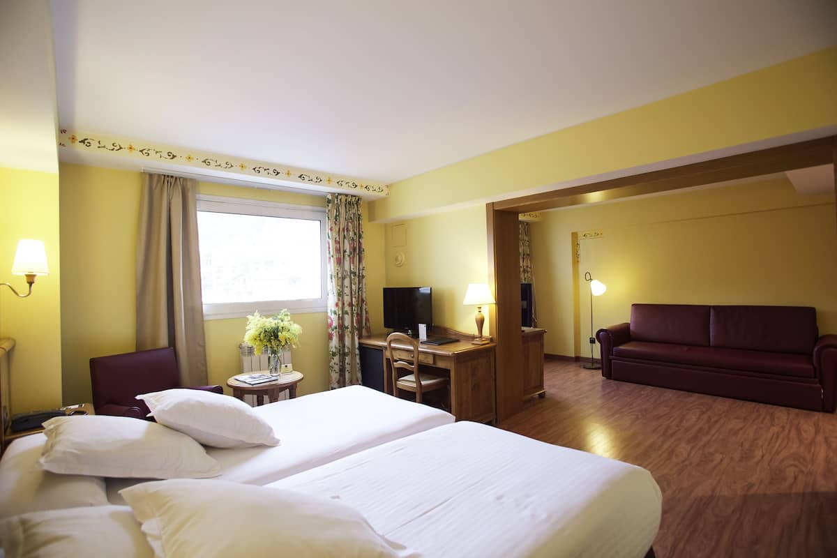 Una habitación de hotel con dos camas, un escritorio con computadora, televisión y sofá.