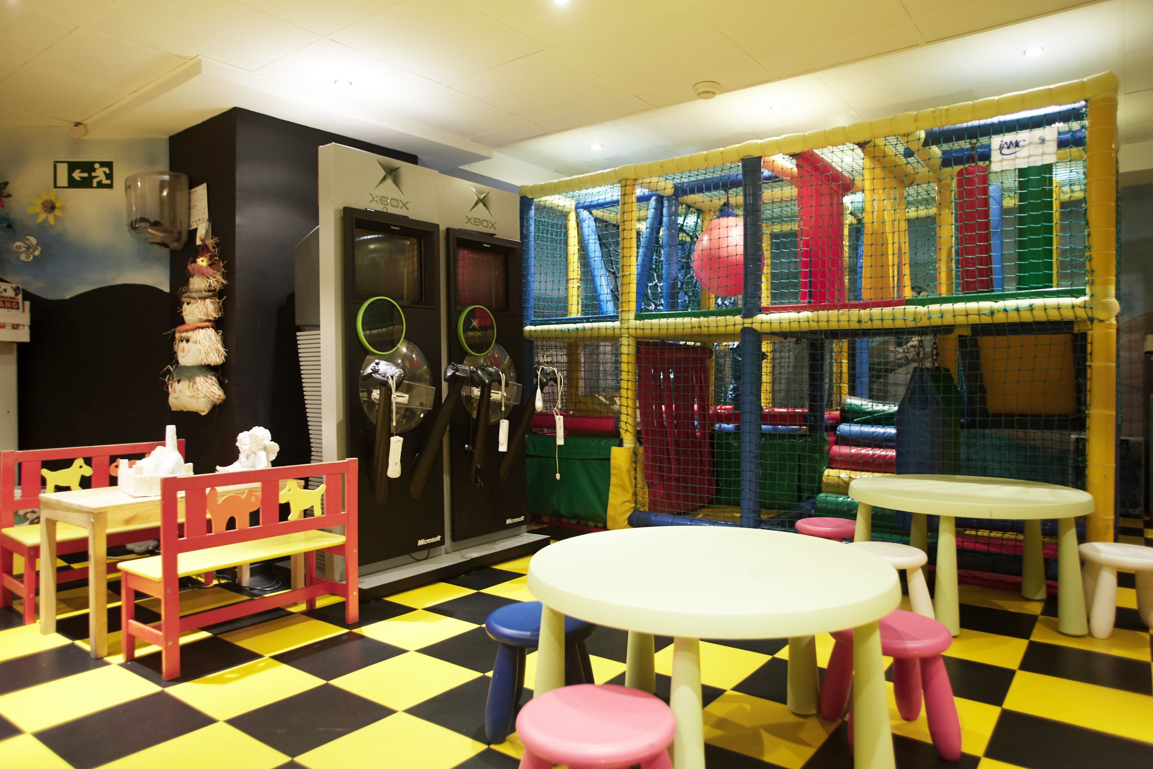 A children's play area with a checkered floor, tables, chairs, and a play structure.