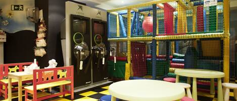 A children's play area with a checkered floor, tables, chairs, and a play structure.