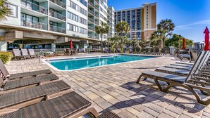 A hotel pool area with lounge chairs, a swimming pool, and a view of the surrounding buildings. - Carolina Dunes (Myrtle Beach)