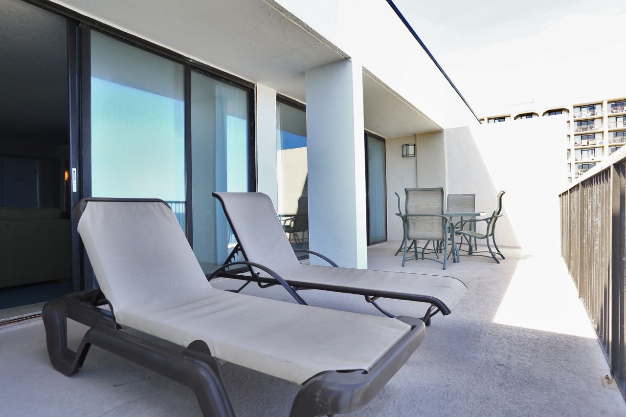 Un balcon avec deux chaises longues, une table avec des chaises et une vue sur un bâtiment en arrière-plan.