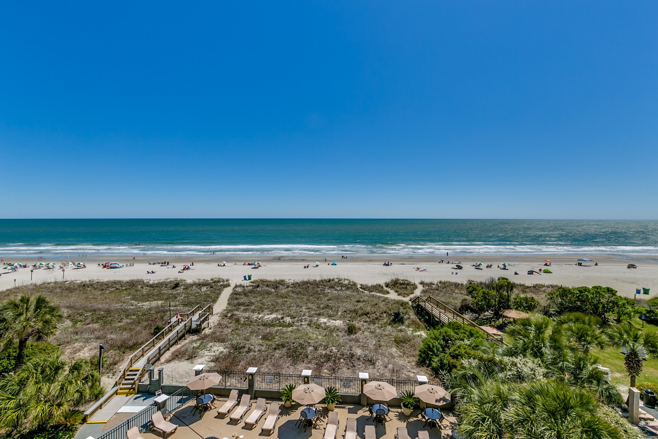 A beach view with a patio area featuring sun loungers and umbrellas.