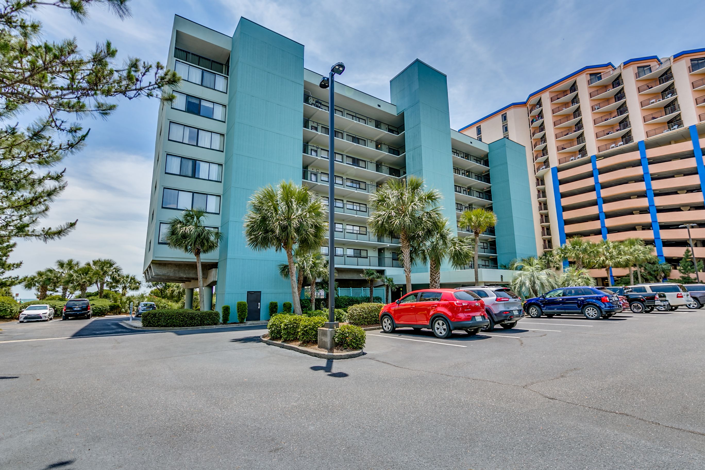 A multi-story hotel with a modern design, featuring a parking lot with several cars.