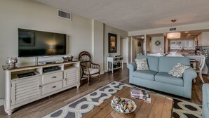 A living room with a television, a sofa, a coffee table, and a dining area with a kitchen in the background. - Carolina Dunes (Myrtle Beach)