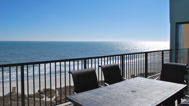 A balcony with a view of the ocean, featuring a table and chairs. - Carolina Dunes (Myrtle Beach)