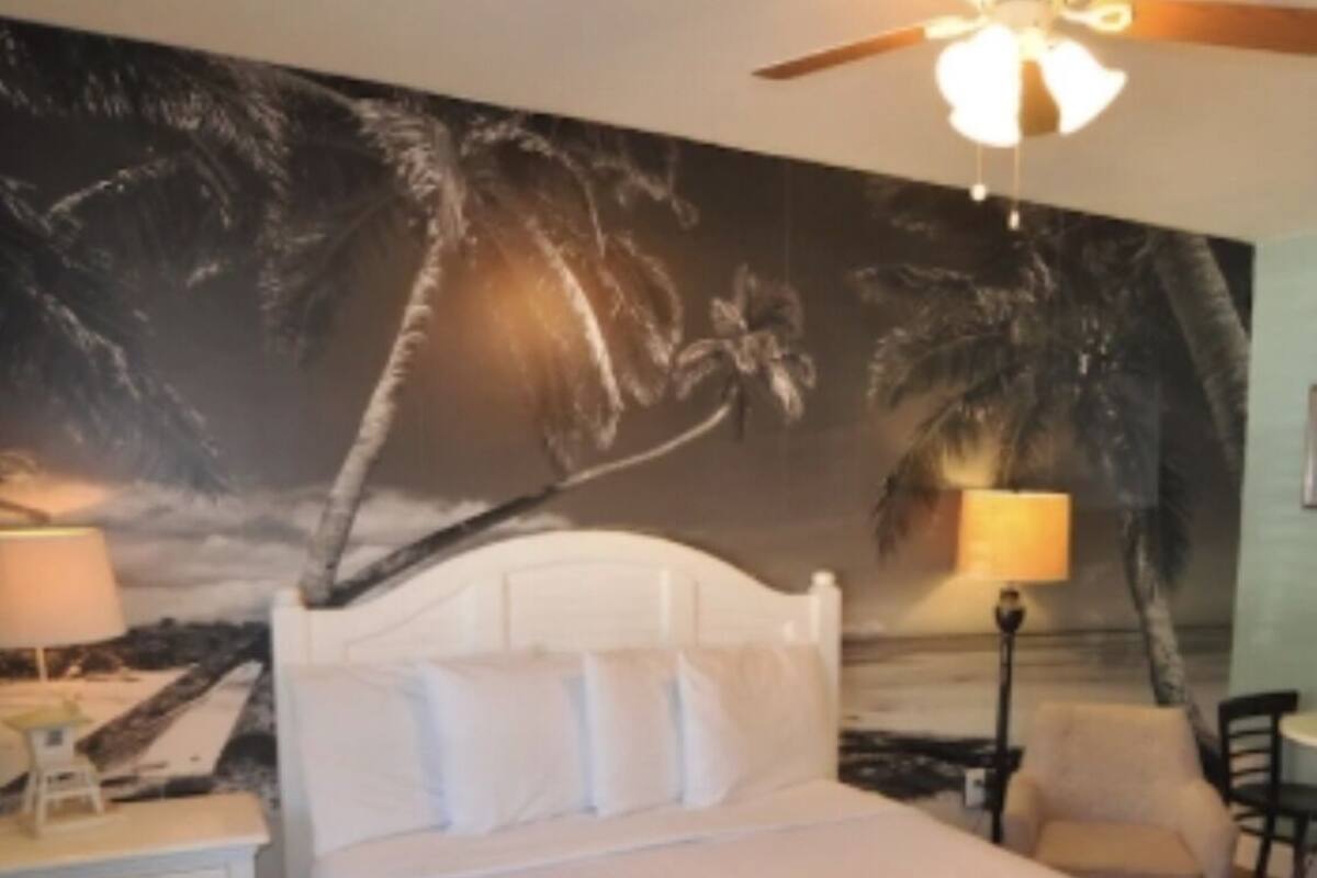 A bedroom with a bed, a ceiling fan, a nightstand, a lamp, and a chair.