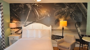 A hotel room with a bed, a chair, a table, and a wall mural of palm trees and a beach. - Lido Islander Inn (Sarasota)