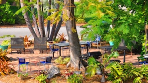 An outdoor seating area with tables and chairs, surrounded by various plants and trees. - Lido Islander Inn (Sarasota)