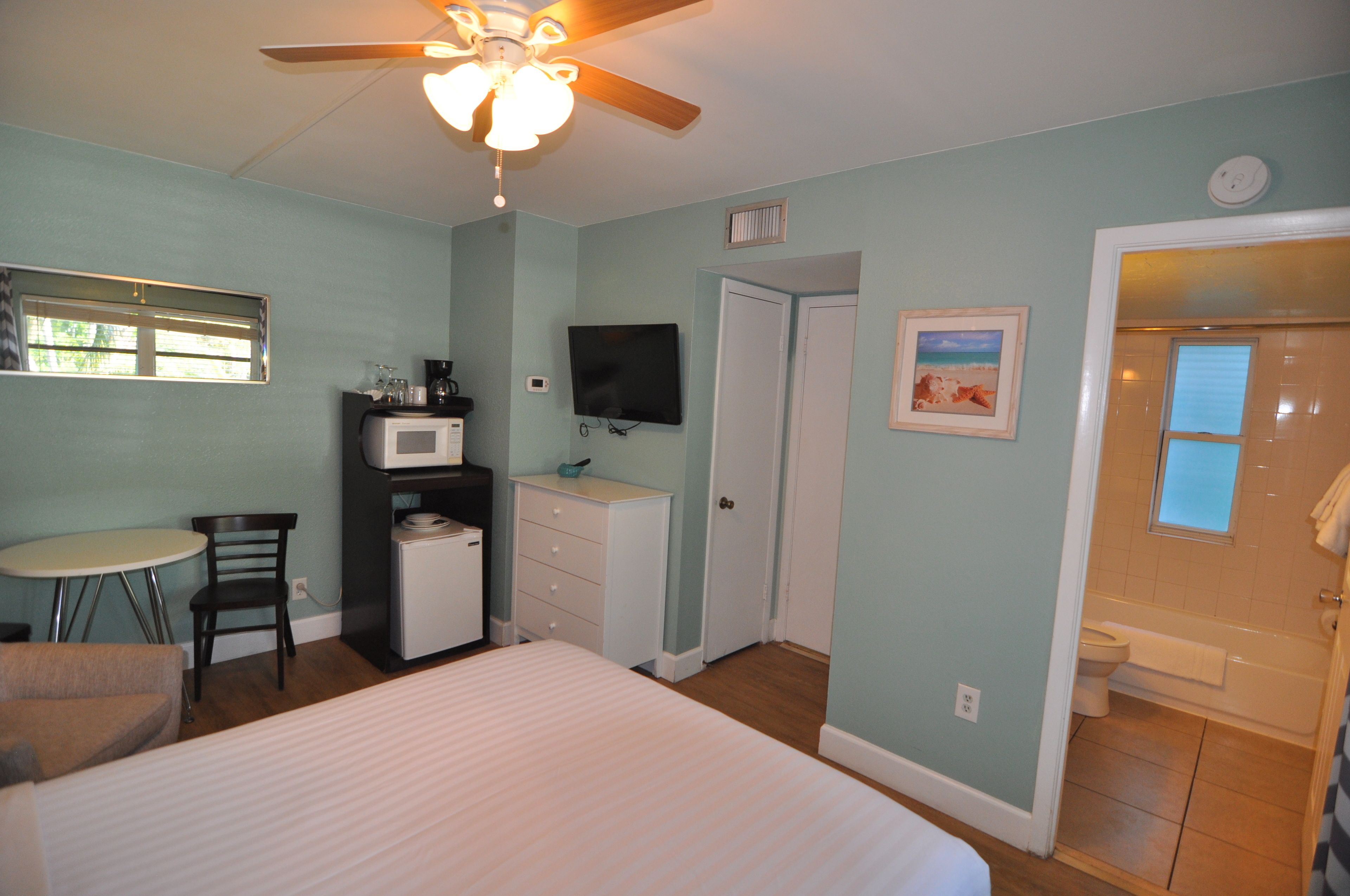 A bedroom with a bed, a desk, a chair, a television, and a door leading to a bathroom.