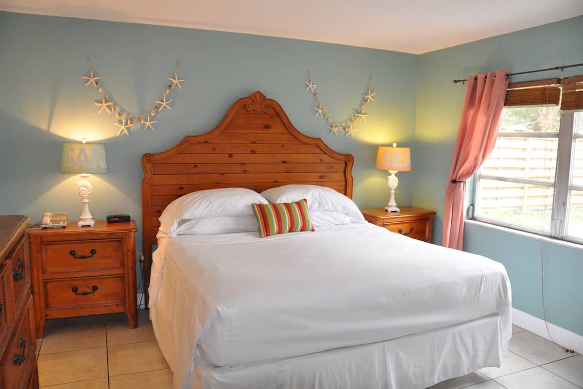 A bedroom with a wooden headboard, a bed with white bedding, two bedside tables with lamps, and star decorations on the wall.