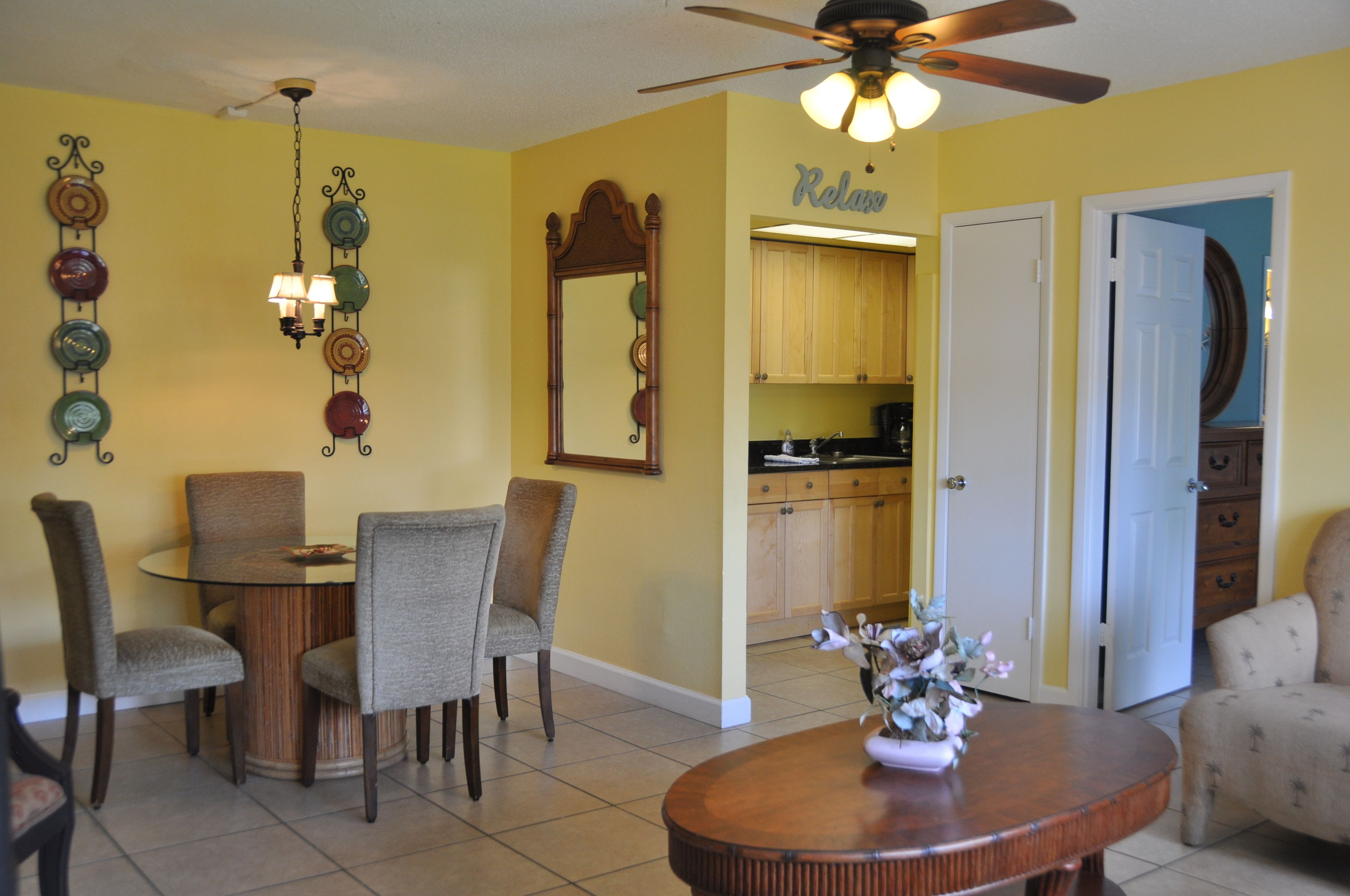 A dining area with a round table and four chairs, a ceiling fan, and a wall-mounted light fixture.