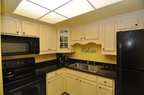 A kitchen with white cabinets, a black refrigerator, a microwave, and a sink.