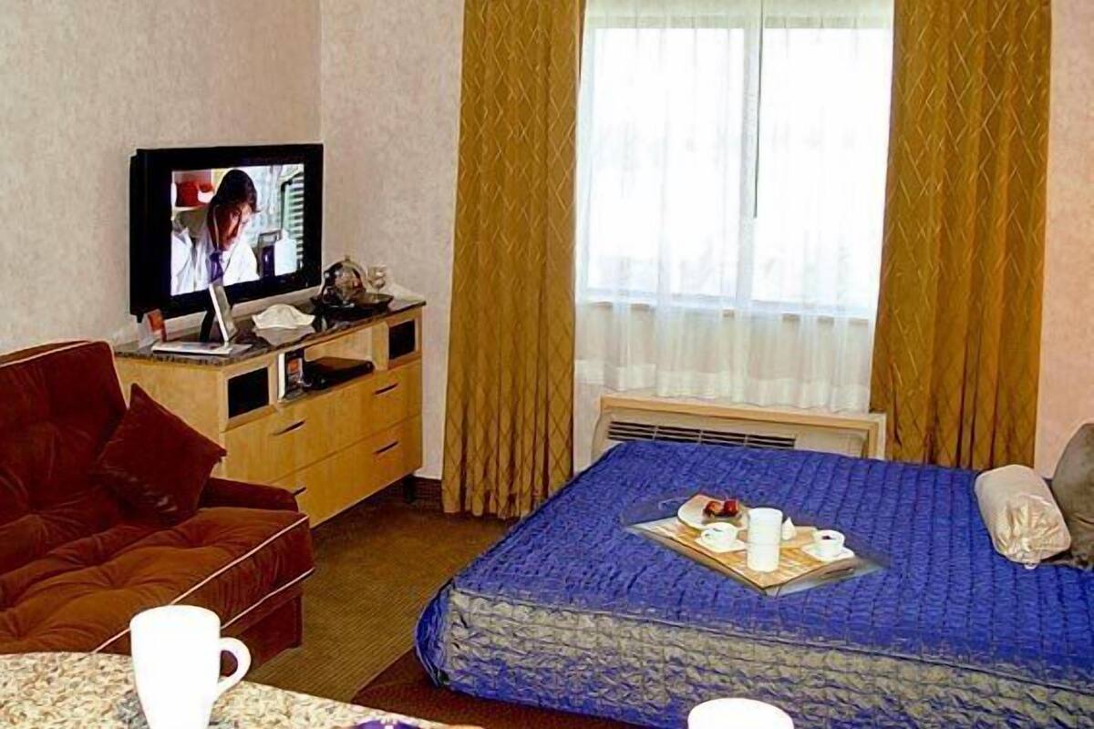 A hotel room with a bed, a TV, a desk with a computer, a chair, and a window with curtains.