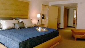 Une chambre d’hôtel avec un grand lit, une table de chevet avec une lampe, une petite table avec un plateau, et un banc en bois.