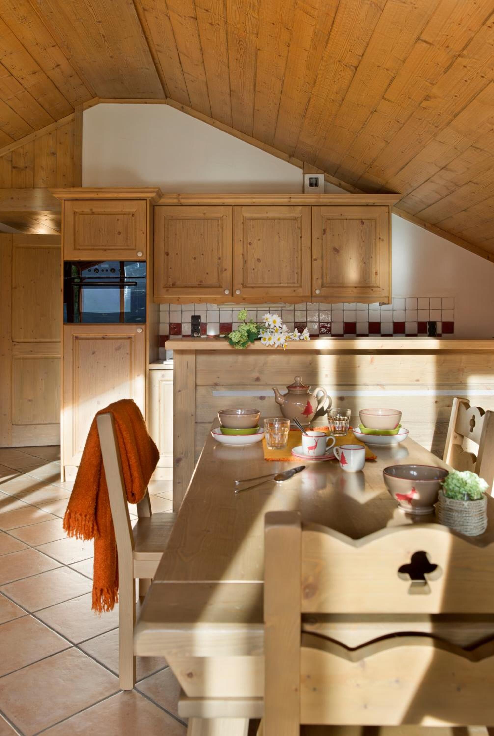 A kitchen with wooden cabinets, a dining table set with dishes, and a view of the living area.