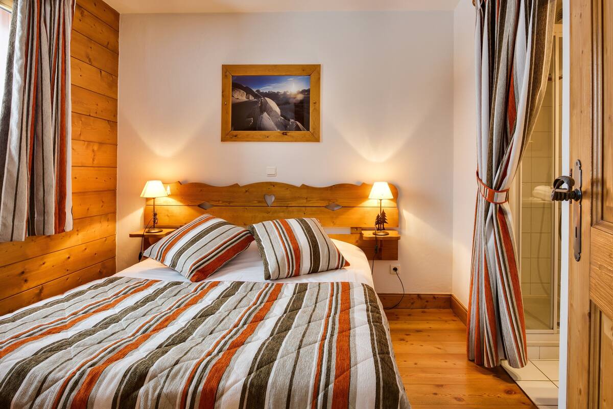 Ein Schlafzimmer mit einem hölzernen Kopfteil, einem Bett mit gestreifter Bettwäsche, zwei Nachttischlampen und einem gerahmten Bild an der Wand.