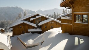 A wooden chalet with a sloped roof, surrounded by snow-covered mountains and trees. - CGH Résidences & Spas Le Hameau du Beaufortain (Villard-sur-Doron)