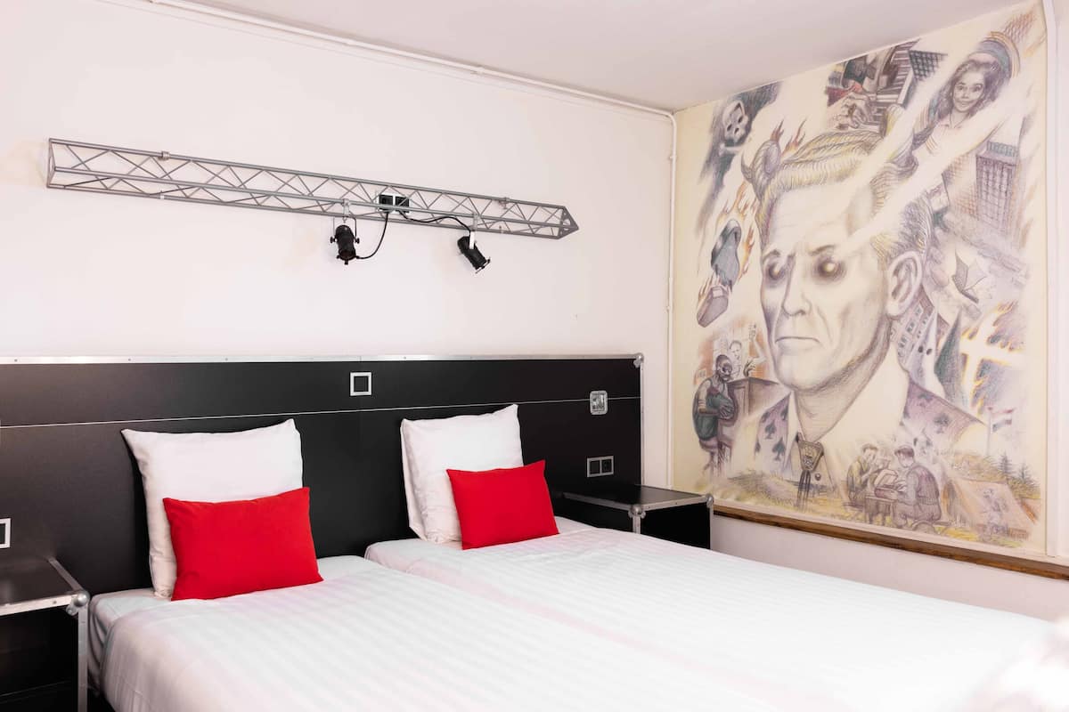 Ein Hotelzimmer mit einem Bett, zwei Nachttischen, einer Wandleuchte und einem großen Wandgemälde.