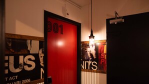 A hallway with a red door labeled '001', a poster with 'US' and 'UNIT' text, and a hanging light fixture. - Backstage Hotel Amsterdam (Amsterdam)