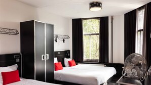 A hotel room with two beds, a wardrobe, a desk with a fan, and a window with curtains. - Backstage Hotel Amsterdam (Amsterdam)