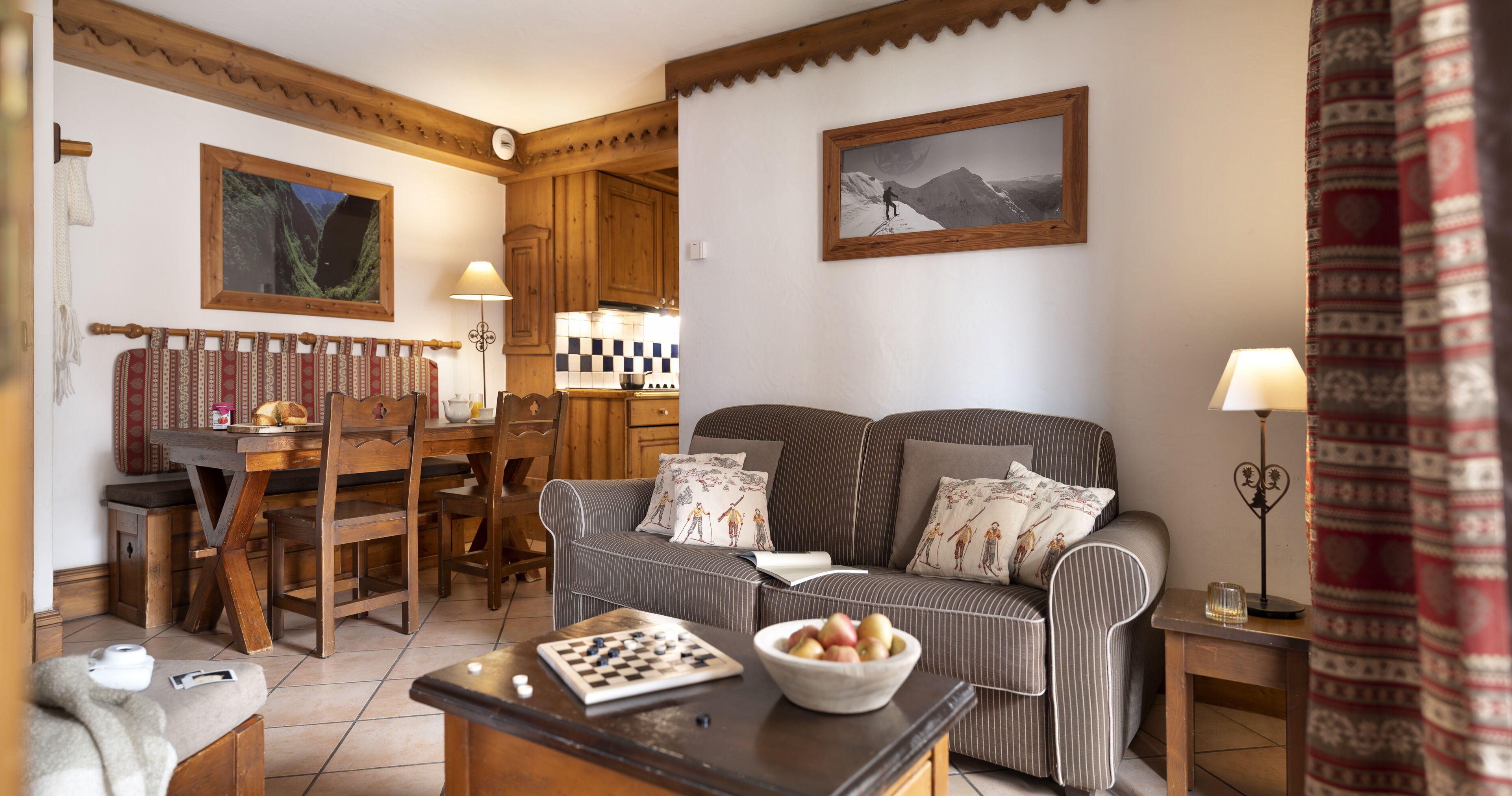 A cozy living room with a sofa, a chessboard, a bowl of fruit, and a dining area with a table and chairs.