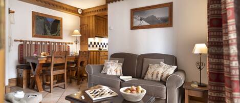 A cozy living room with a sofa, a chessboard, a bowl of fruit, and a dining area with a table and chairs.